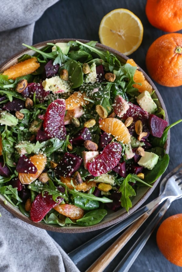 Big ceramic bowl full of greens, citrus fruit, roasted beets, and avocado for a big citrus salad.