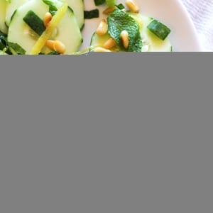 Zesty Cucumber Salad with Pine Nuts on a white plate with green onions and mint leaves and a fork to the side.