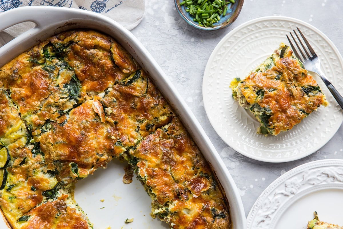 large casserole dish full of breakfast casserole with two plates to the side with slices of casserole, ready to serve.