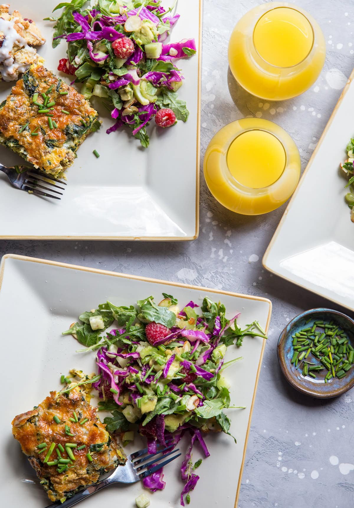 three plates with breakfast casserole and salad with mimosas to the side.