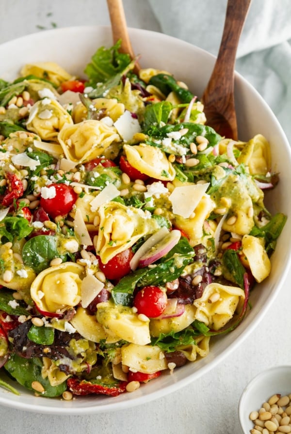Tortellini Salad in a large white bowl with salad tongs ready to serve.