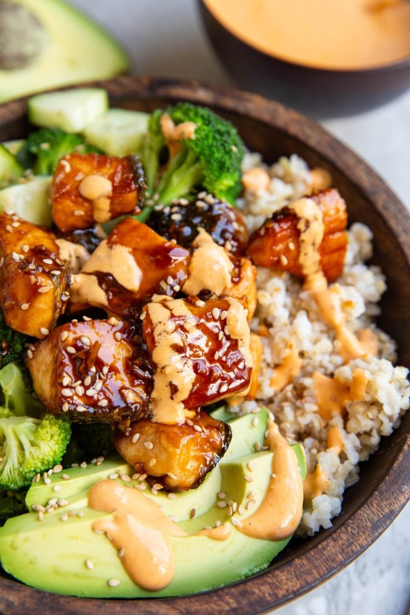 Bang bang salmon in a bowl with avocado, sauteed broccoli, and rice.