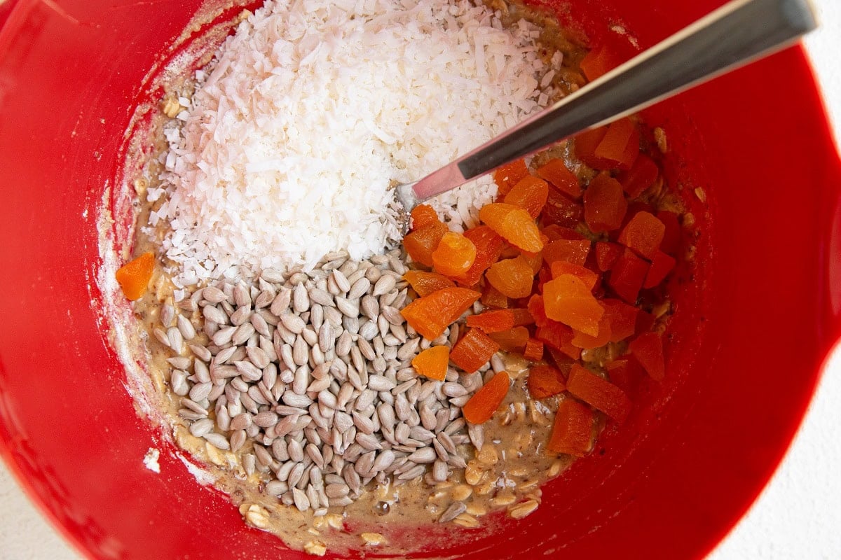 Aussie bite mixture with sunflower seeds, shredded coconut and chopped apricots on top, ready to be mixed in.