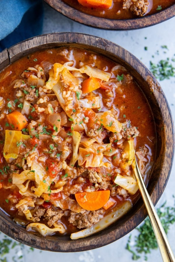 Big wooden bowl of unstuffed cabbage soup with a blue napkin to the side and dried herbs.