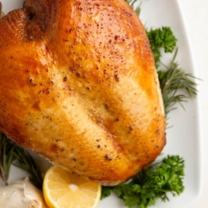 Garlic Herb Roasted Turkey breast on a serving plate with fresh herbs and lemons all around.