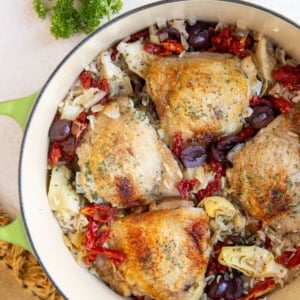 Large pot of chicken and rice with olives, tomatoes, and artichoke hearts.