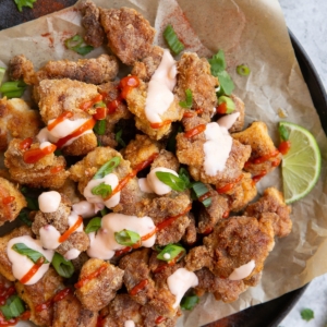 Plate of crispy bang bang chicken drizzled with sauces with fresh lime and cilantro to the side, ready to serve.