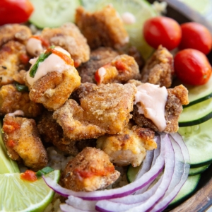 Crispy chicken in a bowl with fresh vegetables and sauce.