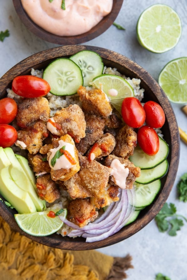 Wooden bowl of crispy chicken, rice, and vegetables.