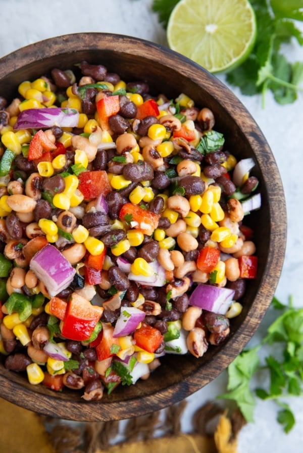 Wooden bowl full of cowboy caviar with a lime and fresh cilantro to the side.