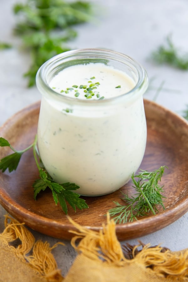 Jar full of homemade ranch dressing with fresh herbs all around.