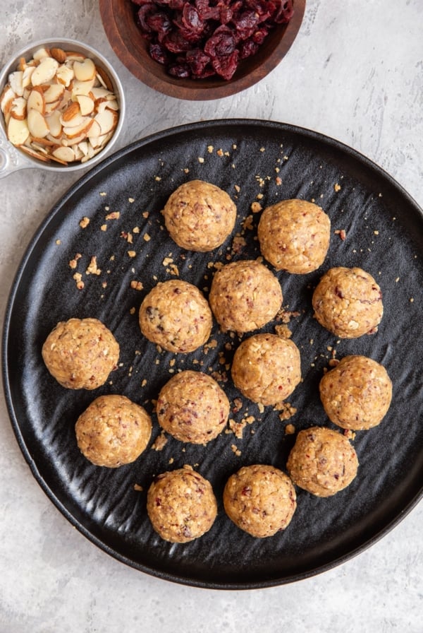 Cranberry Almond Protein Balls on a black plate with a bowl of dried cranberries and almonds to the side.