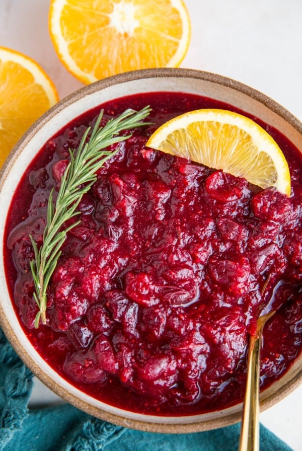 Orange ginger cranberry sauce in a bowl with fresh oranges and a blue napkin to the side.