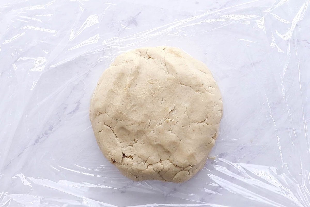 Gluten free sugar cookie dough on a sheet of plastic wrap, ready to go into the refrigerator.