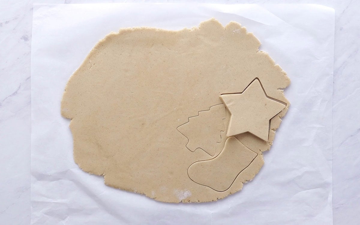 Gluten free cookie dough rolled out into a flat shape with cookie cut out shapes to make sugar cookies.
