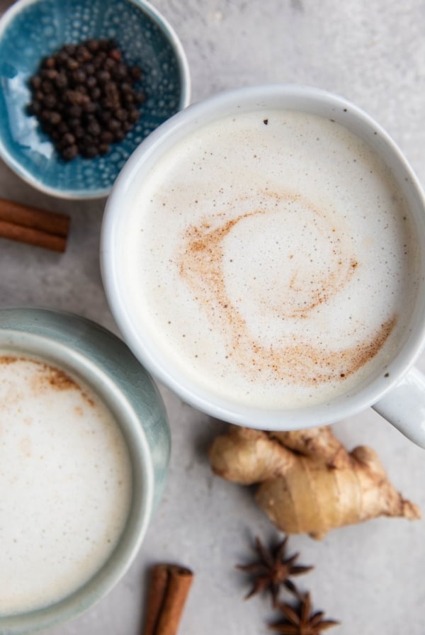Two chai lattes on a table with spices all around, ready to drink.