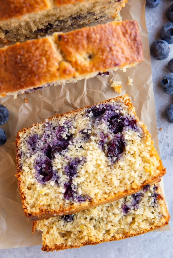 Lemon blueberry protein bread cut into slices on parchment paper with fresh berries all around.