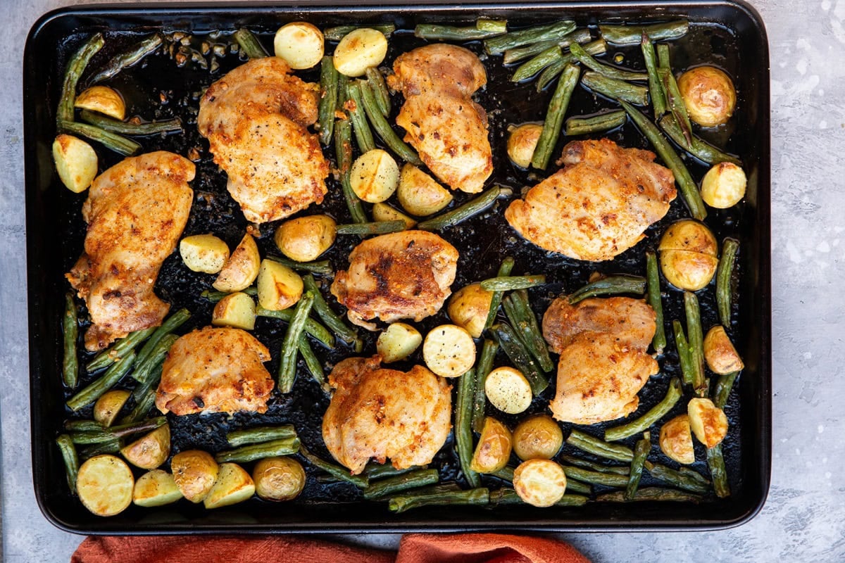Large sheet pan with vegetables and chicken thighs, fresh out of the oven and ready to serve.