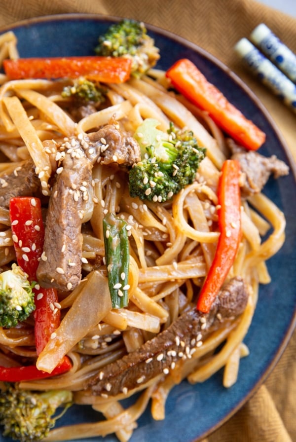 Blue plate with beefy noodles and veggies with chopsticks to the sides.