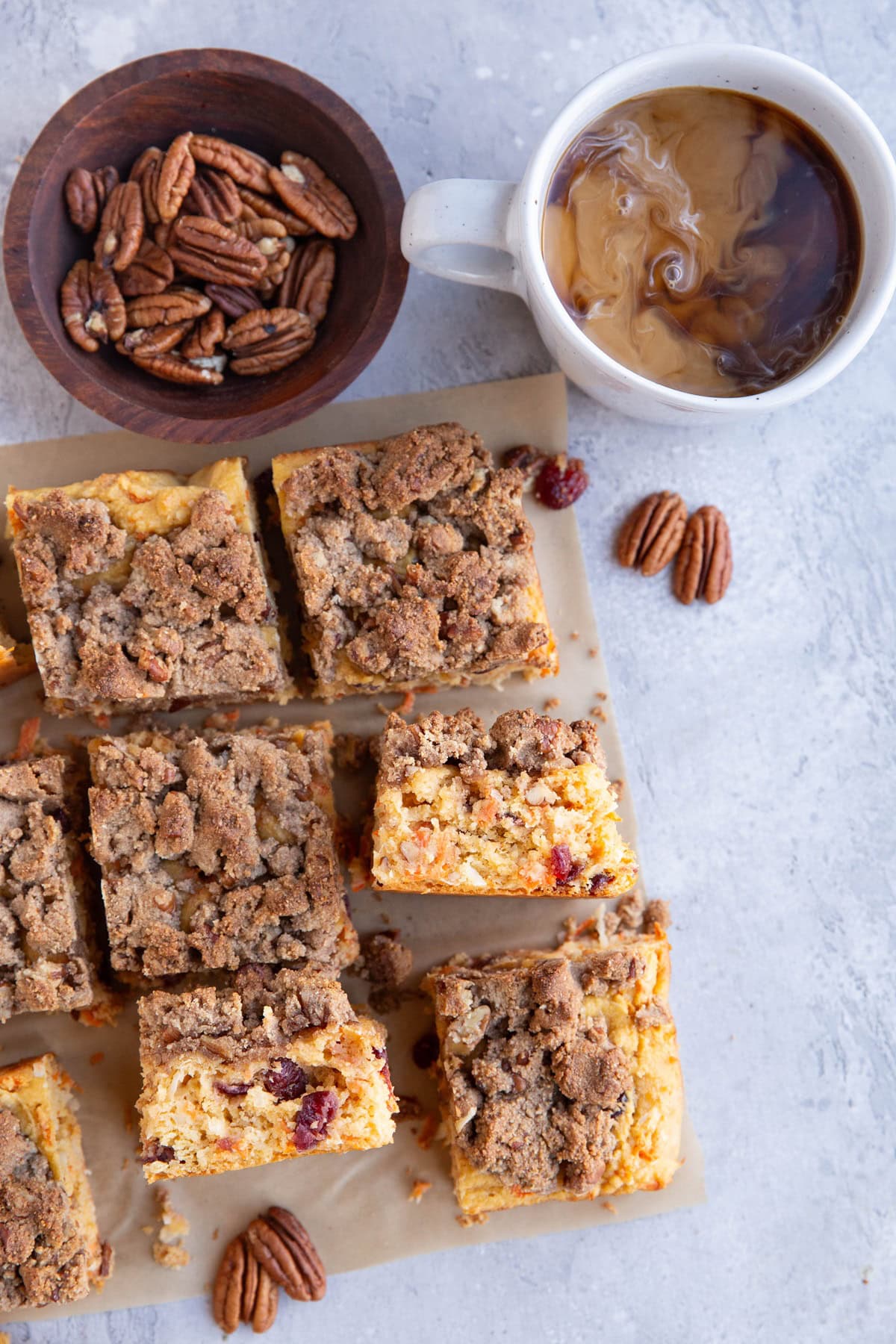 Carrot cake coffee cake cut into slices with a bowl of pecans and a mug of coffee with cream swirling in the coffee.