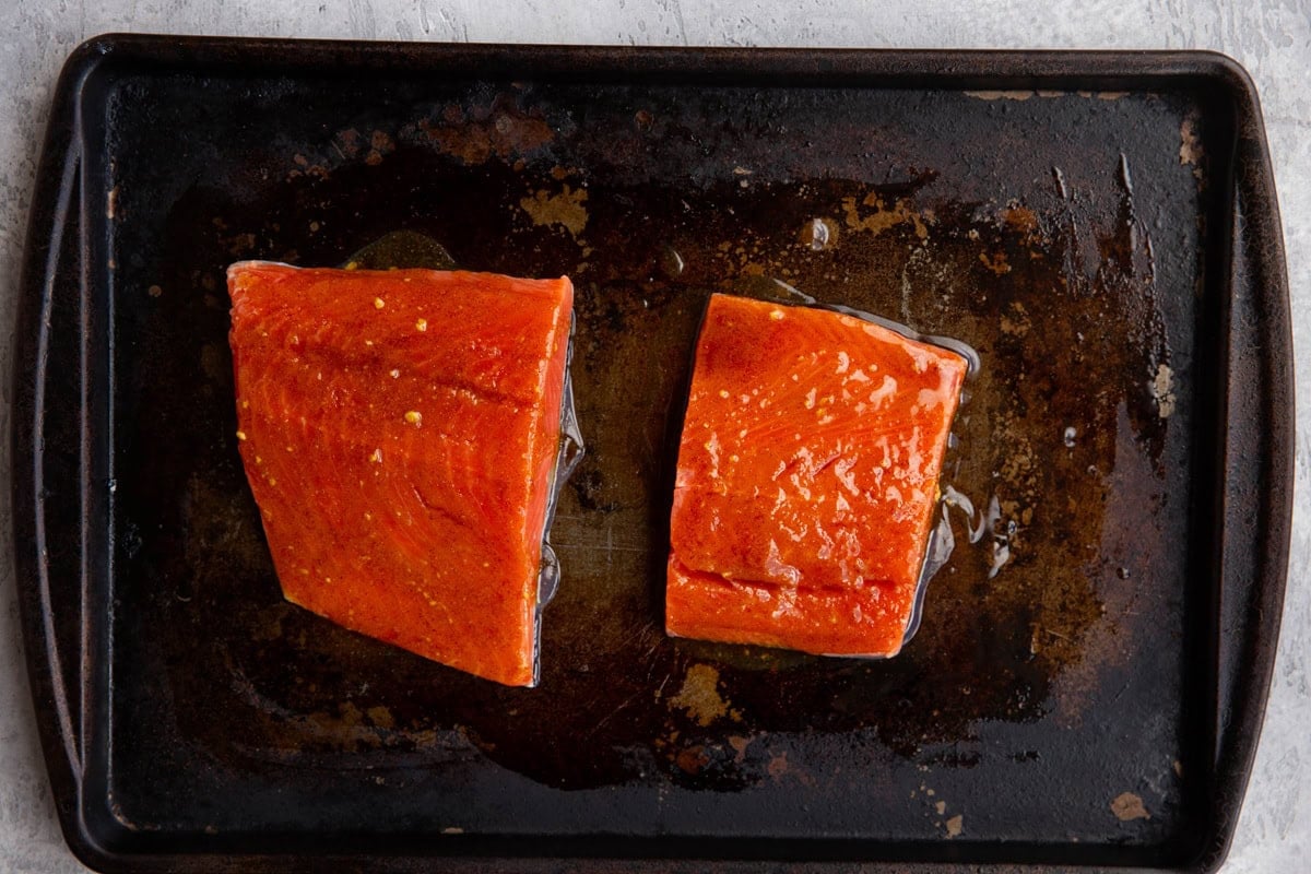 Two salmon filets on a baking sheet in a spice mixture marinade.