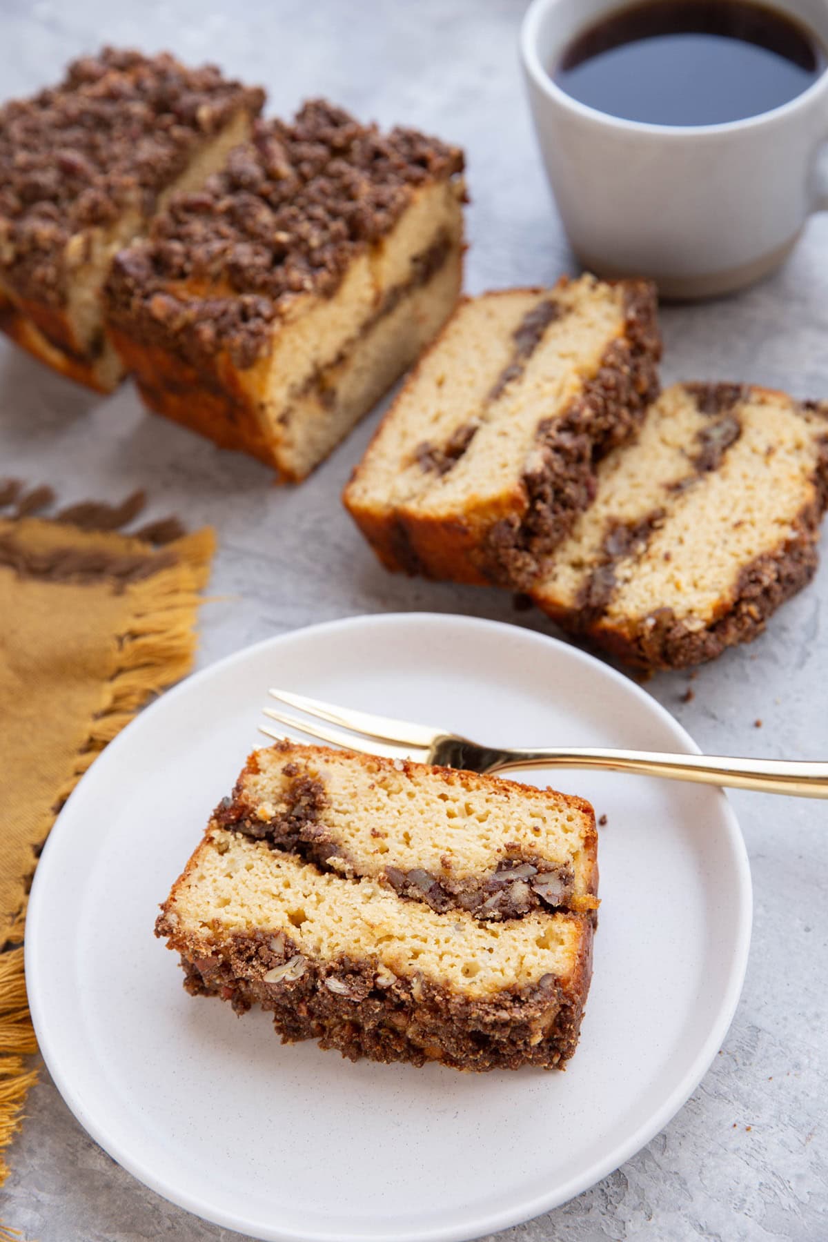 Slice of cinnamon roll bread on a plate with the rest of the loaf in the background and a mug of coffee.