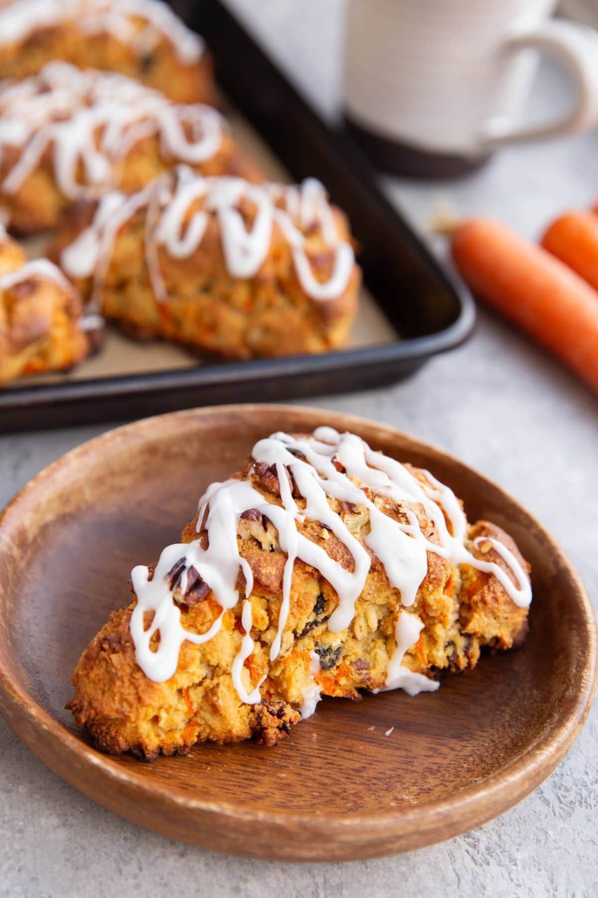 Carrot scone on a wooden plate with the rest of the scones in the background.
