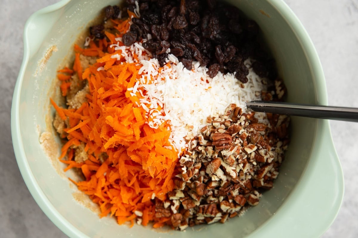 Mixing bowl with shredded carrot, pecans, coconut, and raisins on top of scone dough.