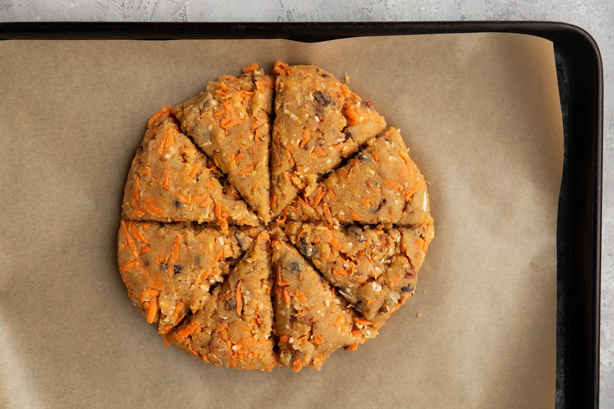 Baking sheet with carrot scone dough cut into triangles in the shape of a disc.