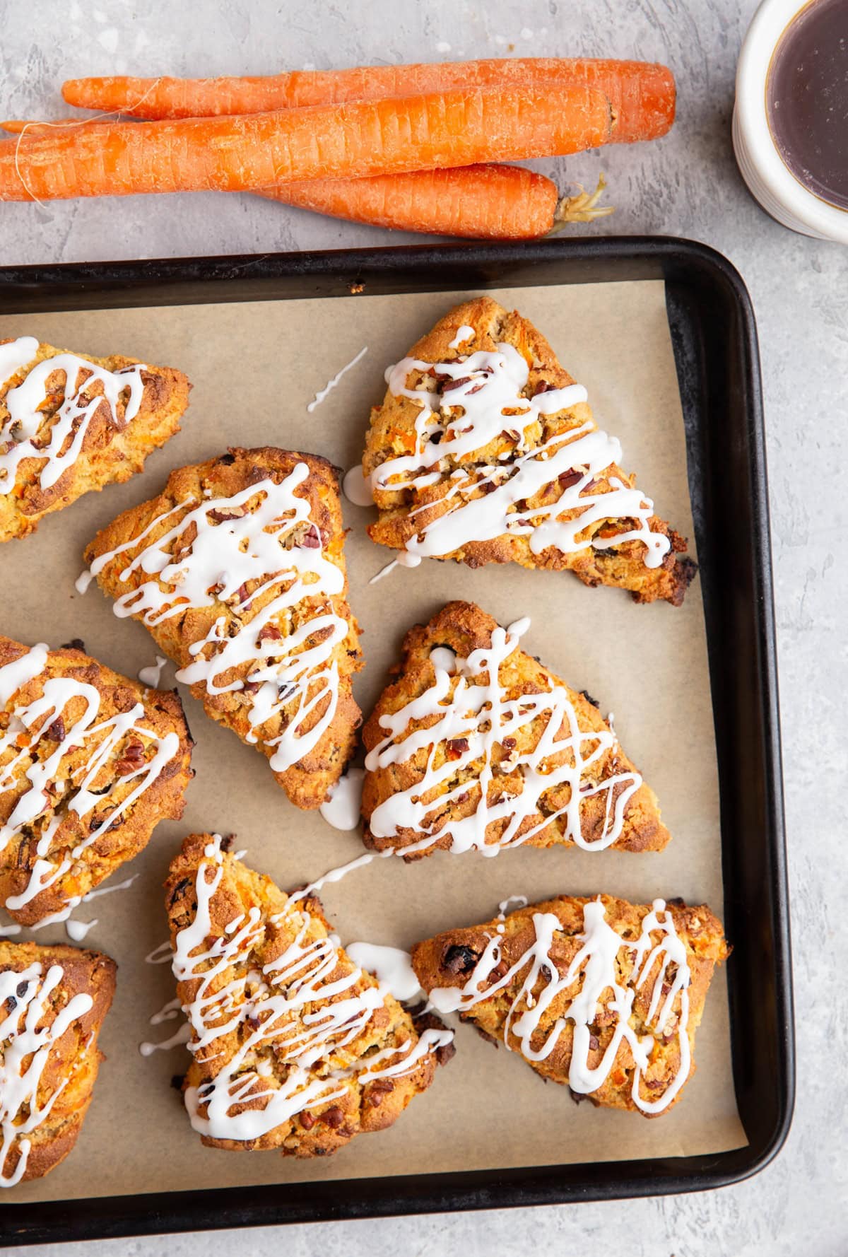 Cookie sheet of scones with fresh carrots and a mug of coffee to the side.
