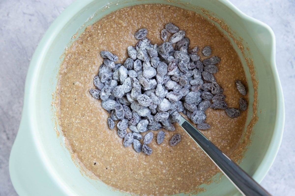 Mixing bowl with bread batter and floured raisins on top, ready to be mixed in.
