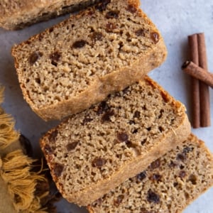 Loaf of cinnamon raisin bread cut into thick slices with cinnamon sticks to the side.