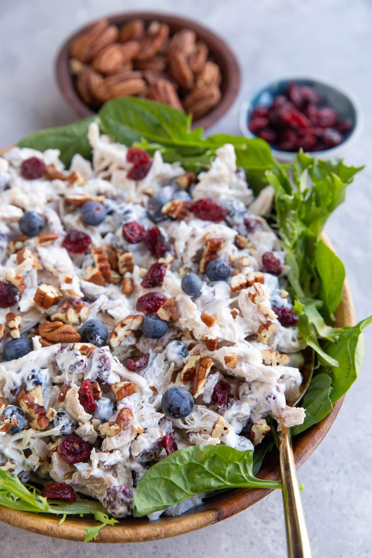 Cranberry Pecan Chicken salad on top of a bed of greens inside of a wooden bowl with a golden serving spoon to the side.