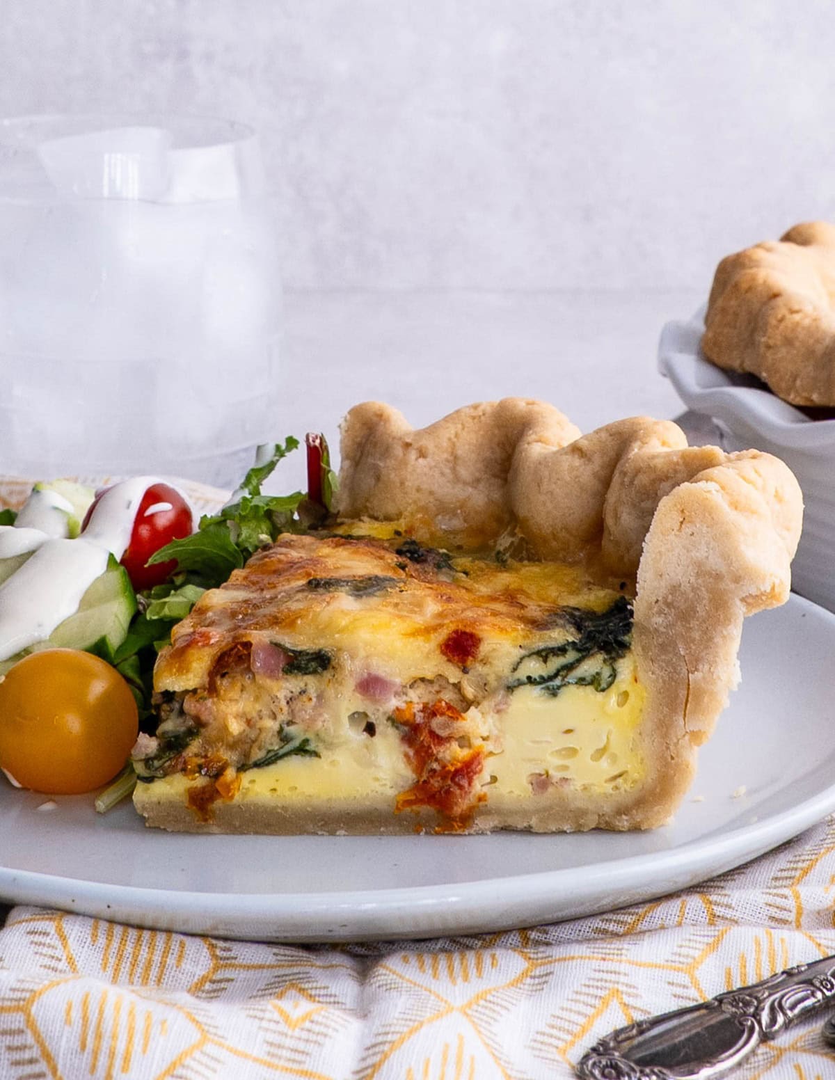 Slice of quiche with the rest of the quiche in the background.
