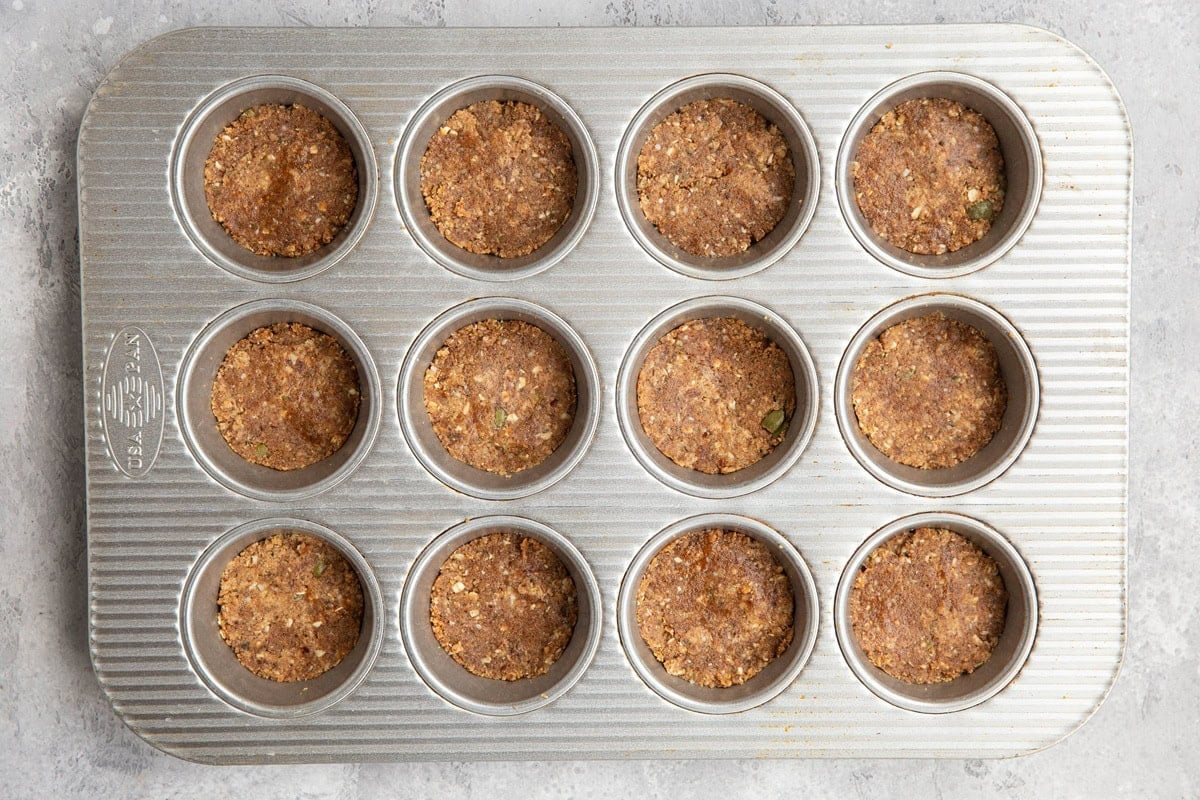 Muffin tray with energy bite mixture inside, pressed into even layers.