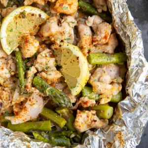 Chicken, asparagus, and lemons cooked in a foil packet. Foil packet is open to reveal the finished result.