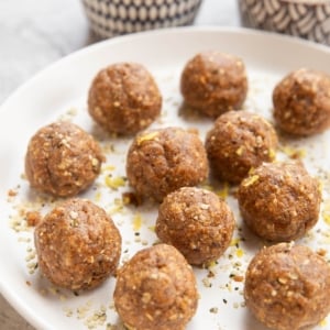 Plate of energy balls sprinkled with lemon zest. Two bowls of balls and seeds in the background.
