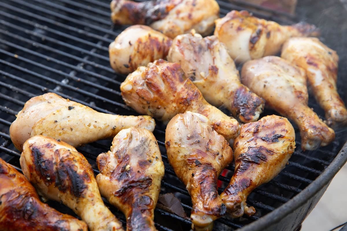 Charcoal barbecue with chicken drumsticks grilling. Golden brown char marks on the chicken legs.