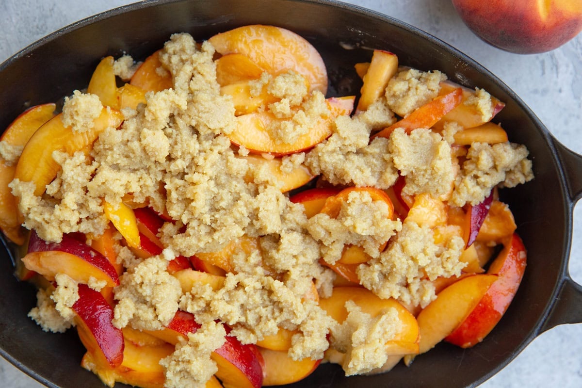 Baking dish with peach filling and crumble topping on top, ready to go into the oven to bake.