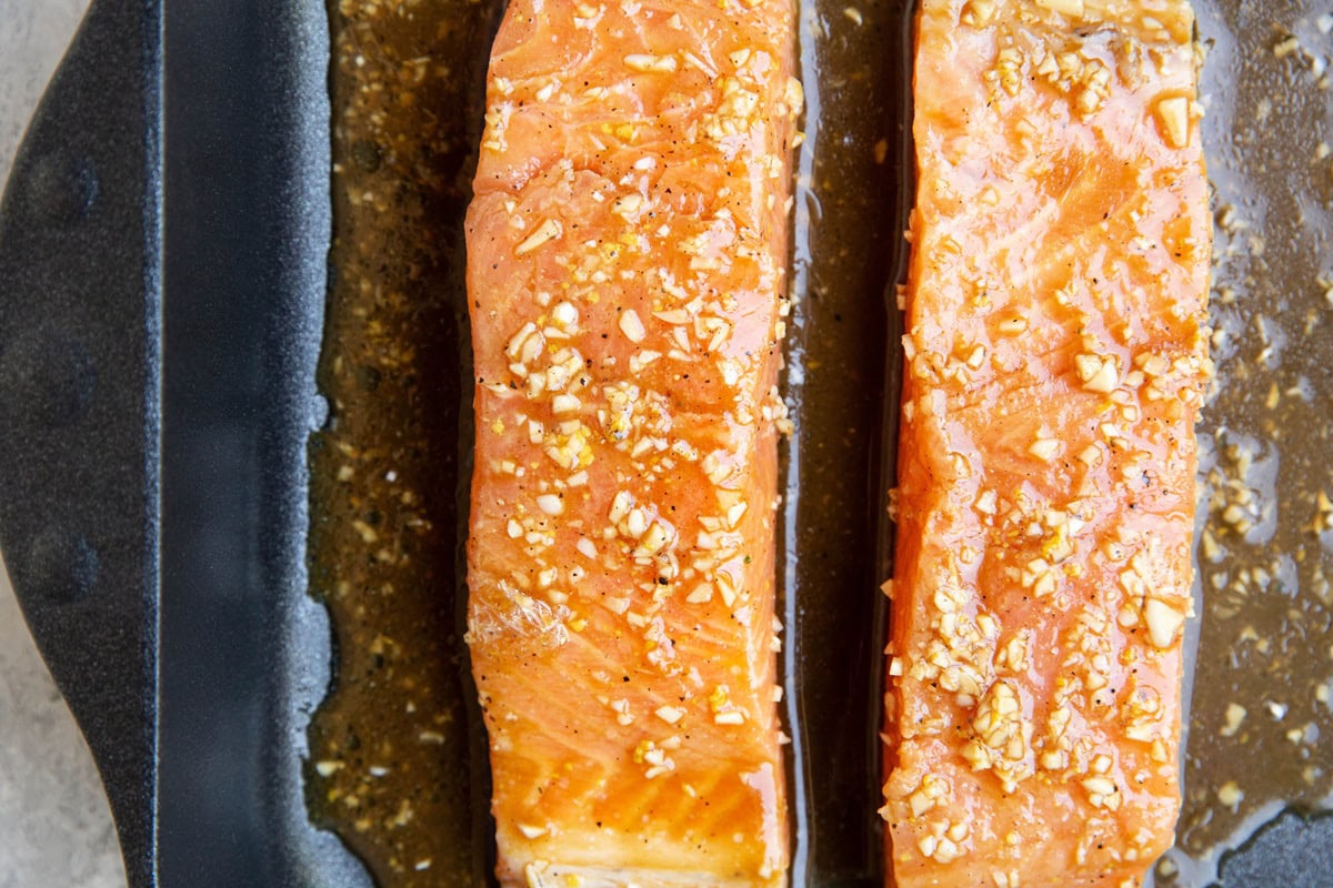 Two marinated salmon filets in a large baking dish, ready to go into the oven.