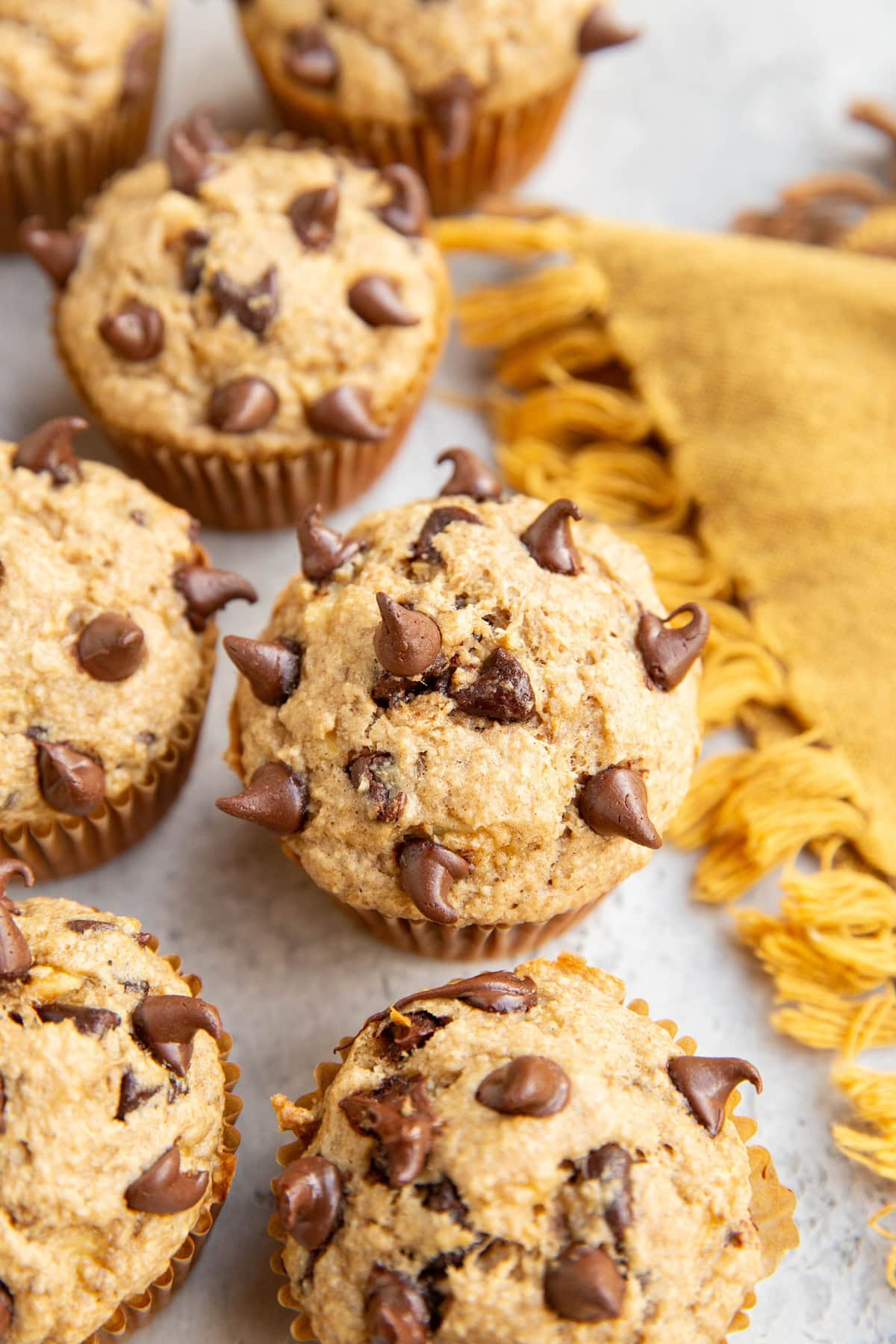 Many banana oat muffins on a surface with a golden napkin to the side. Fresh out of the oven and ready to eat.