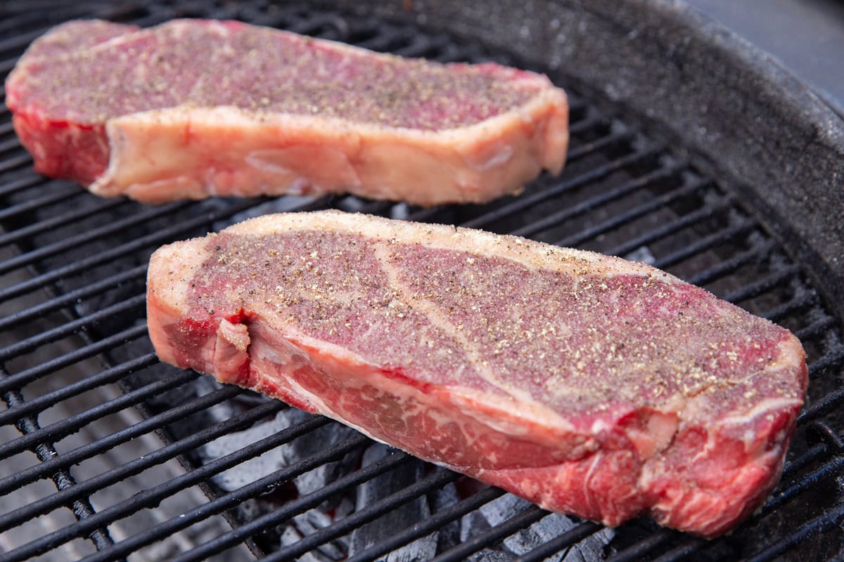 Raw steaks on a grill that are seasoned over coals.