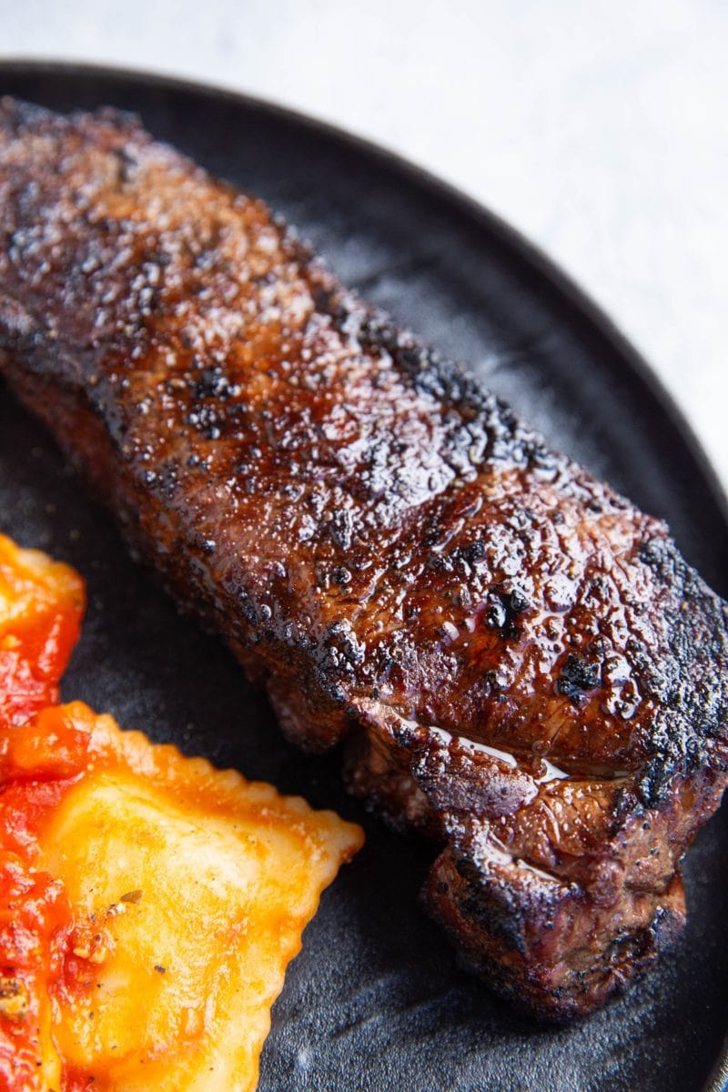 Plate of grilled new york strip steak with raviolis as a side dish.