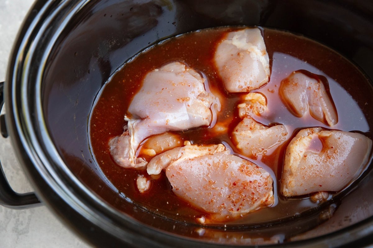 Crock pot full of raw chicken thighs and birria sauce.