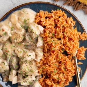 Chicken in a creamy sauce on a blue plate with Mexican rice and a golden fork, ready to serve.