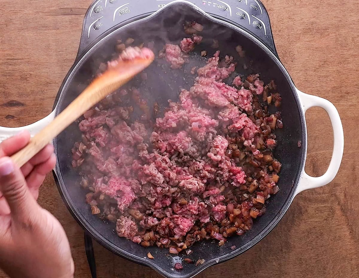 Ground beef in a skillet with mushrooms and onions, being cooked into the mixture.