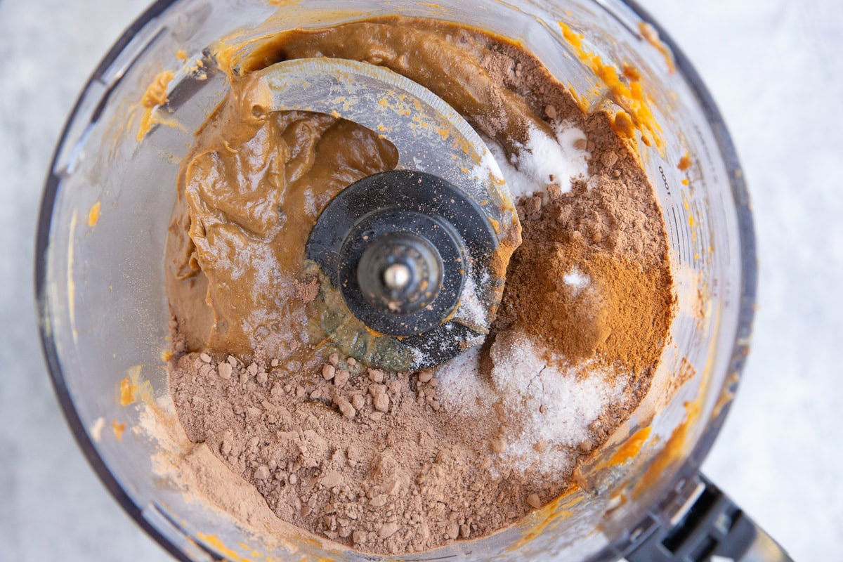 Food processor full of wet ingredients for brownies with the dry ingredients on top, ready to be mixed in.