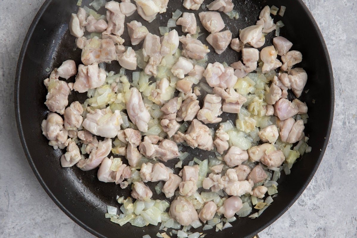 Large skillet with chopped chicken thighs and onion sautéing to make a pasta recipe.