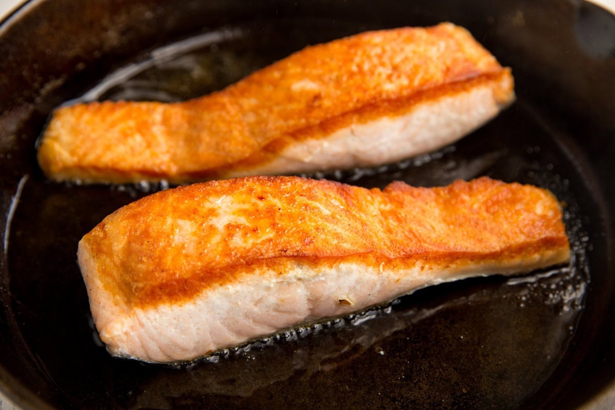 Seared salmon in a cast iron skillet with golden brown tops.
