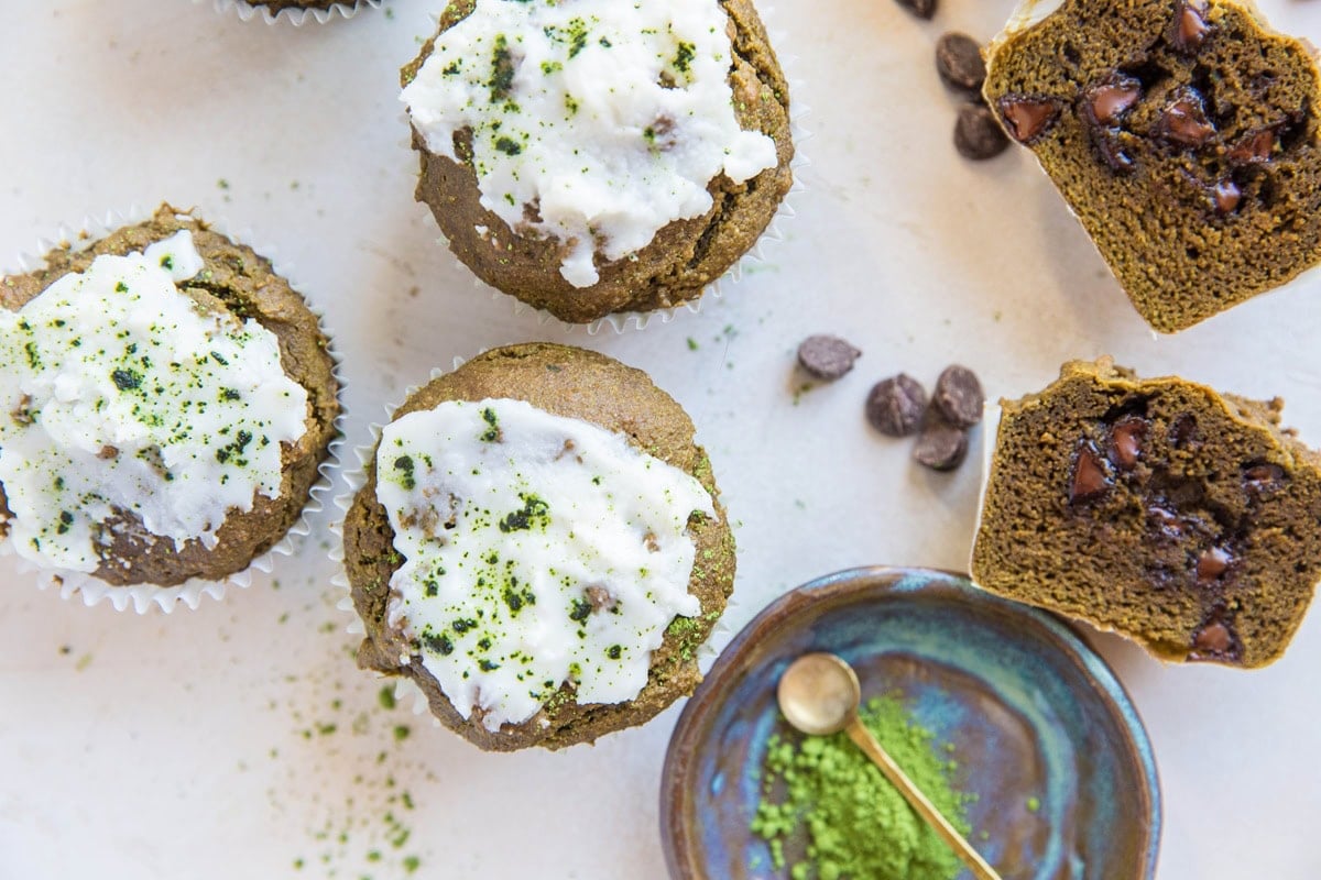 A matcha muffin cut in half to expose chocolate chips on the inside and more matcha muffins to the side.